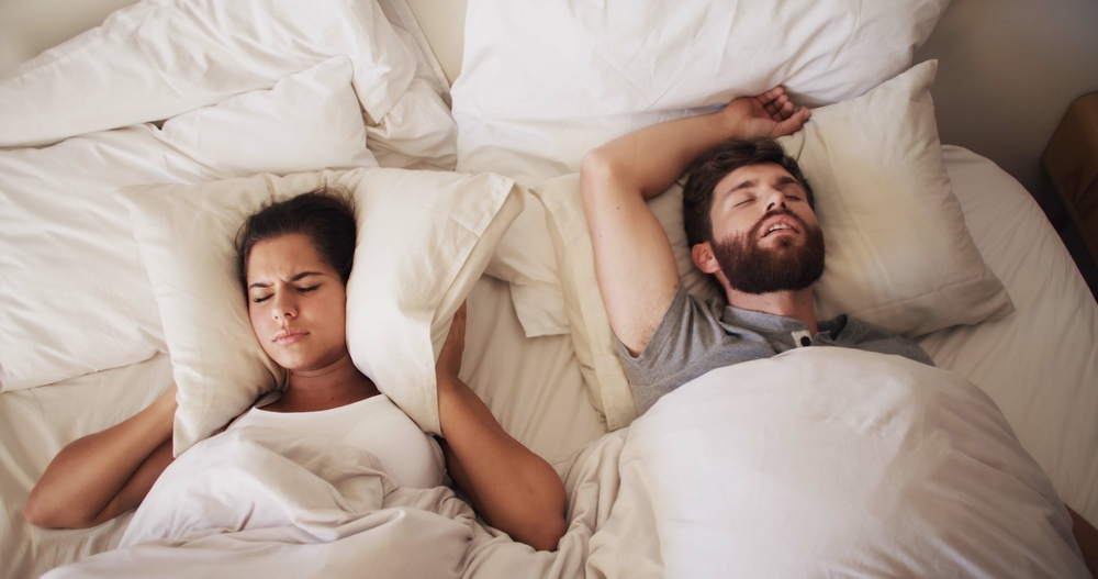 Couple experiencing disrupted sleep from snoring and possible sleep apnea in bed